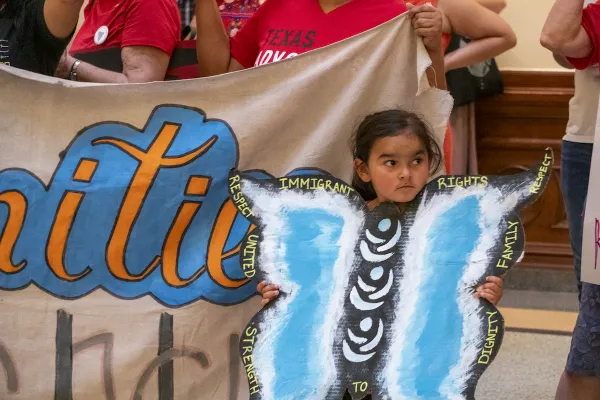 Girl stands with a butterfly sign at an immigration rally